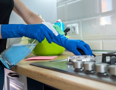 Woman cleaning stainless steel gas surface in the kitchen with rubber gloves.