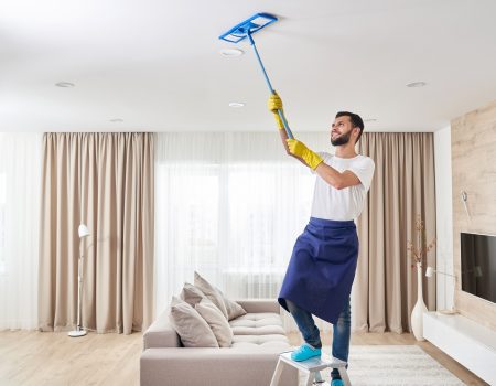 Man holding mop pile, cleaning ceiling in living room.