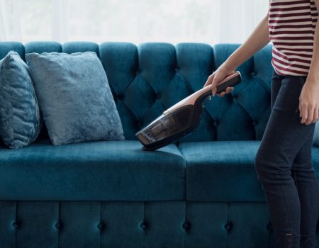 Close up of A woman housewife vacuuming furniture in a house with a hand-held portable vacuum cleaner